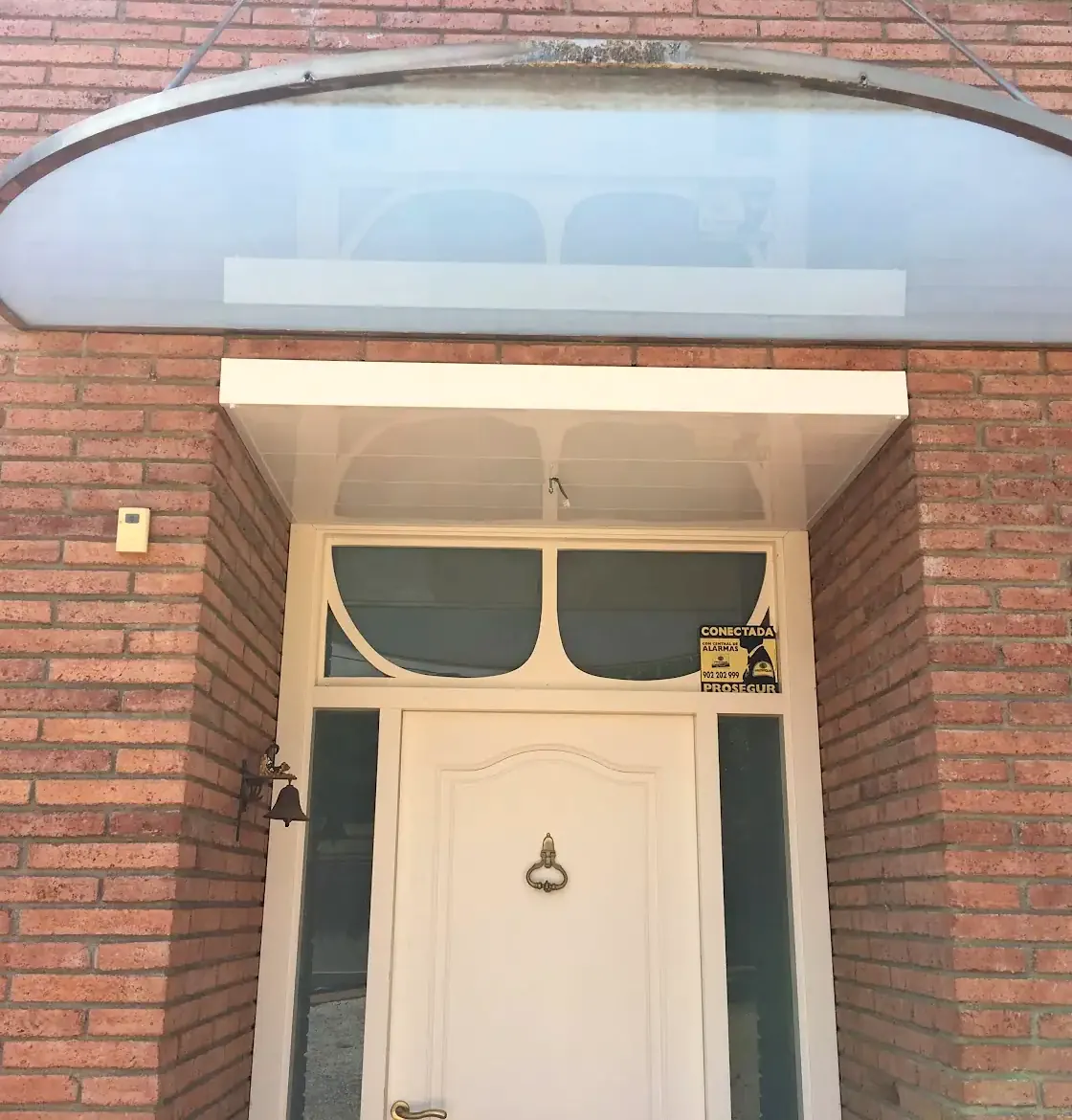 Entrada de una casa de ladrillo con marquesina blanca y vidrieras alrededor de la puerta