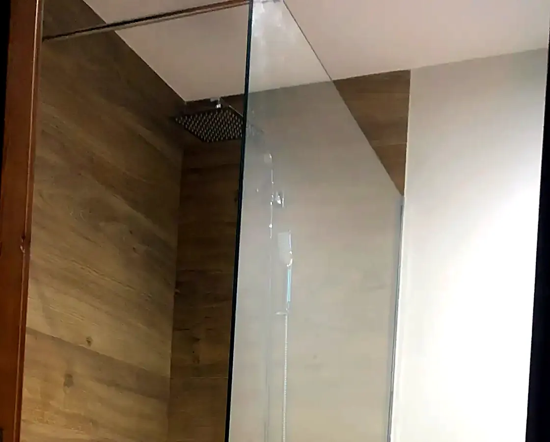 Mampara de ducha de vidrio fijo en un baño con pared imitación madera